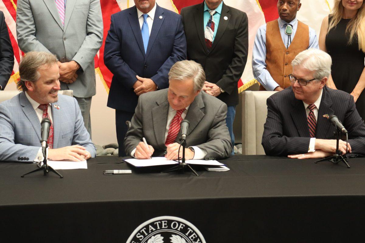 Governor Greg Abbott signing a bill surrounded by other representatives.