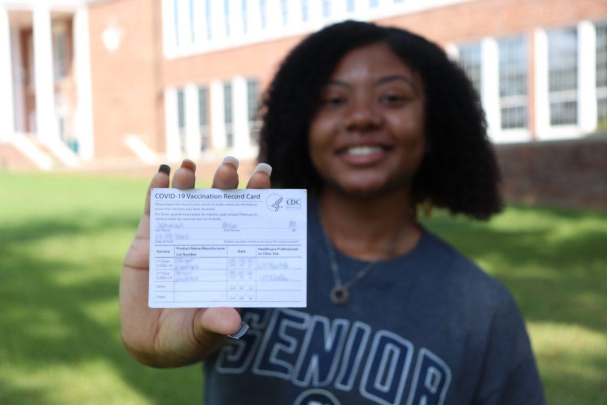 Student smiling holding their vaccine card
