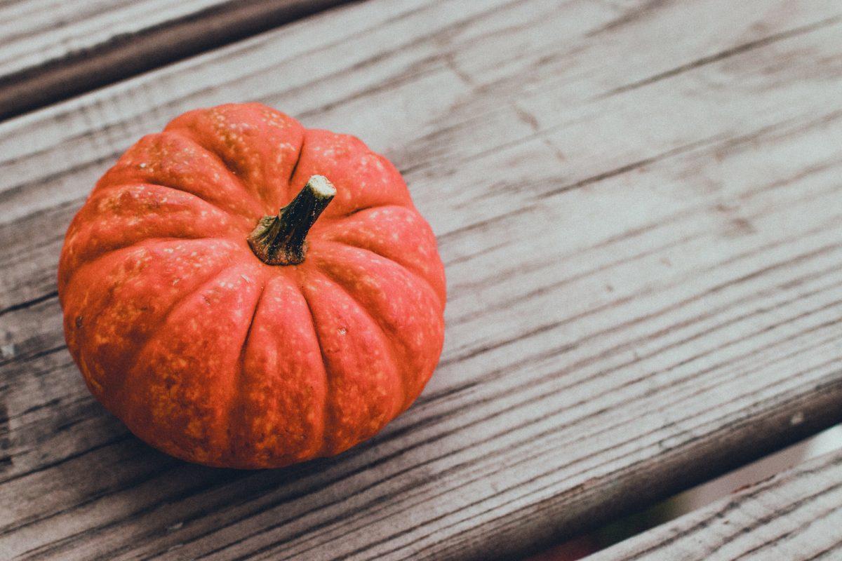 A small orange pumpkin sitting on wood