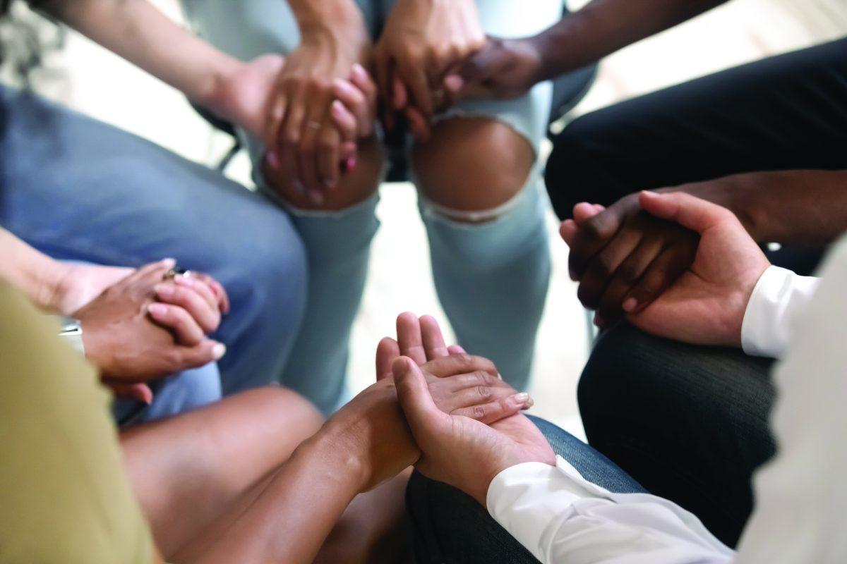Diverse people sitting in circle holding hands at group therapy session, religious christian team pray together for recovery give psychological support, counseling training trust concept, close up