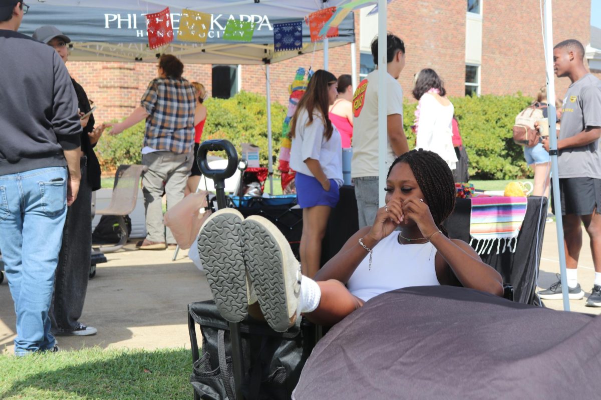 Apache Cheer Janiya McCarty (Health science) takes a break in a wheelbarrow under the shade of the Apache Cheer tent.